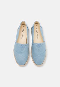 Zapatillas de slip-on de color azul claro con parte superior de lona y suela de yute trenzado. Presenta un detalle de costura en forma de V y un suave forro interior.
