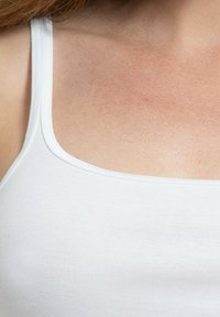 Top in cotone bianco con spalline sottili e una texture a costine, collo a giro e superficie liscia.
