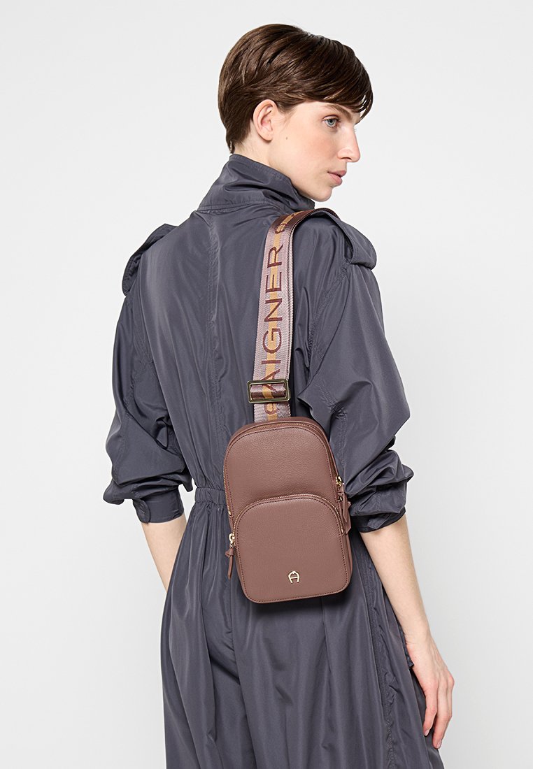 Braune Leder-Crossbody-Tasche mit glatter Textur. Verfügt über zwei Reißverschlussfächer und einen Trageriemen mit Branddetails.