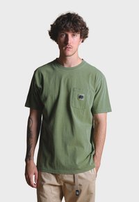 Olive green cotton t-shirt with crew neck, short sleeves, and a chest pocket featuring a black elephant design. Relaxed fit.