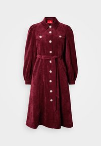 Burgundyszínű bársonyruha gallérral, hosszú puffos ujjakkal és elülső zsebekkel. Díszes gombos részletek és illő deréköv.