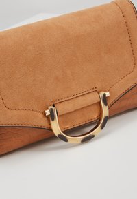 Pochette en daim et cuir beige tan présentant une texture lisse, un motif croco marron, et un accent en métal doré avec des taches foncées.