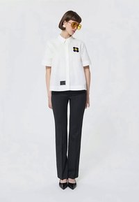 Λευκό κοντομάνικο πουκάμισο με ένα λουλούδι, συνδυασμένο με μαύρο κομμένο παντελόνι και μαύρα μυτερά παπούτσια. Περιλαμβάνονται κιτρινα υπερμεγέθη γυαλιά ηλίου.