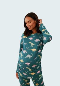 Långärmad pyjamasuppsättning i teal-färgad tyg med färgglada dinosauriemönster i rosa, grönt och gult. Mjuk material med avslappnad passform.