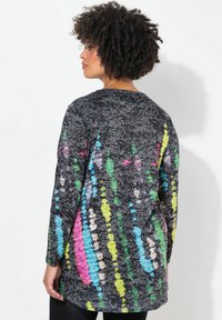 Tunique à manches longues en tissu noir avec un aspect texturé, présentant des éclaboussures multicolores vives en rose, vert, bleu et jaune.