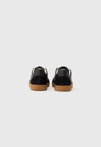 Black leather and suede sneakers with a gum sole, featuring a minimalist design and contrasting cream accents on the back.