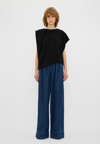 Top nero oversized a maniche corte con scollatura drappeggiata, abbinato a pantaloni in denim blu a gamba larga con orlo rifinito e texture sottile.