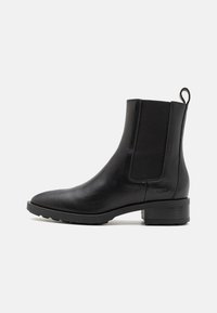 Černá kožená kotníčková bota s elastickými bočními panely, špičatou špičkou a nízkým blokovým podpatkem. Obsahuje zadní poutko pro snadné obouvání.