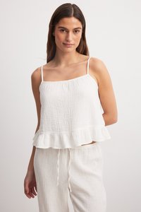 Weißes, ärmelloses Oberteil mit strukturiertem Finish und Volant-Saum. Kombiniert mit passenden, leichten Hose mit Kordelzug aus einem ähnlichen Stoff.