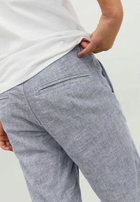 Harmaat pellavahousut, joissa on tekstuuripinta, takatasku ja rento malli, yhdistetty valkoiseen puuvillateepaitaan.