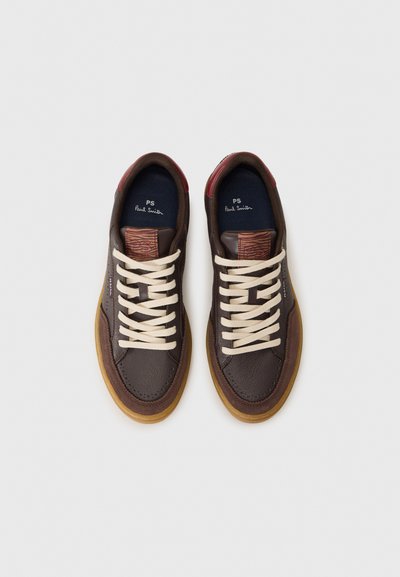 Baskets en cuir marron avec des lacets beiges, comportant un accent texturé bordeaux au niveau du talon et une semelle en caoutchouc gomme. Marque discrète visible.
