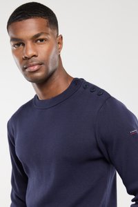 Dunkelblauer Strickpullover mit Rundhalsausschnitt, vier Knopfdetails an einer Schulter und figurbetontem Schnitt. Glatte Textur.