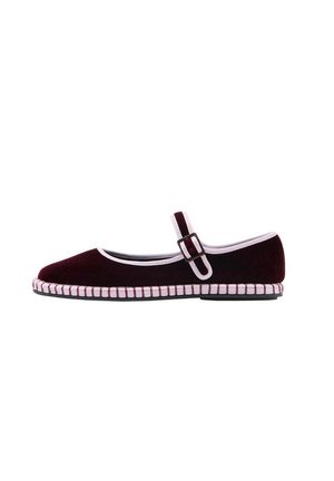 Zapato Mary Jane individual de color rojo oscuro con ribete blanco, correa ajustable con hebilla y detalles cosidos a lo largo de la suela sobre un fondo blanco.