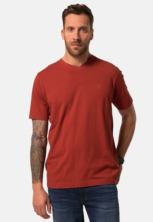 Rød v-hals t-shirt i bomuldsstof med korte ærmer, der har et subtilt logo print på venstre bryst. Sammen med mørke jeans.