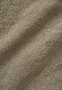 Tissu beige texturé avec des motifs de tissage visibles et de légers plis créant des ombres douces à la surface.