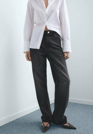 Jeans negros de pierna ancha hechos de mezclilla, combinados con una camisa blanca de botón. El conjunto se complementa con unos tacones marrones de punta.
