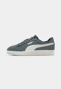 Šedé semišové tenisky Puma s bílým logem a podrážkou, černými tkaničkami a brandingem Puma na boku a patě.