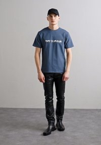 Mėlynas medvilninis marškinėlis su baltu užrašu "THE KOOKS", derinamas su siaurais juodais odiniais kelnėmis ir juodais auliniais batais. Paprastas kepurė.