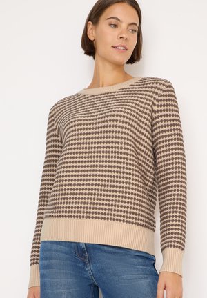 Maglione lavorato a maglia beige con motivo a pois marroni, collo rotondo, orlo e polsini a coste. Abbinato a jeans blu.