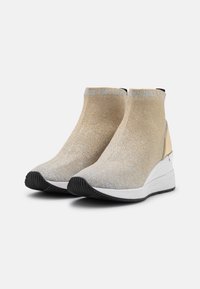 Baskets compensées avec un dessus en maille dorée métallique, semelle blanche et semelle extérieure en caoutchouc noir ; elles présentent un élastique à la cheville et un logo subtil au niveau du col.