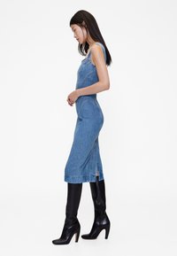 Traper haljina uskog kroja i duljine do koljena, s bočnim prorezima. Nošena s crnim kožnim čizmama s potpeticom do koljena za kontrast.