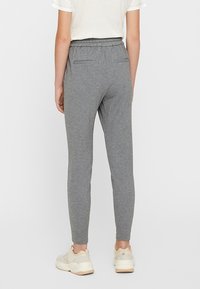 Grå träningbyxor med en mjuk textur, smal passform, elastisk midja och två bakfickor, tillsammans med ljusa sneakers.