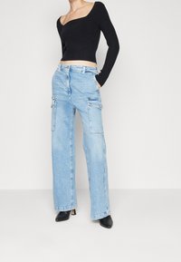 Sort ribbet langærmet cropped top kombineret med lyseblå vidbenede cargobukser med lommer, båret med sorte støvler med hæl.