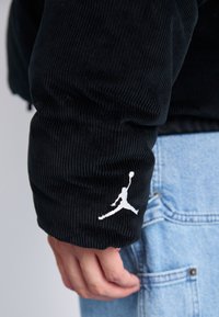Manica di giacca in velluto nero con finitura testurizzata, caratterizzata da un logo Jumpman bianco. Il design include una vestibilità comoda e polsini a costine.