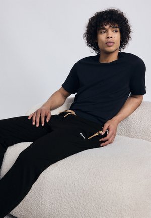 Schwarzes T-Shirt mit kurzen Ärmeln, kombiniert mit schwarzen Sweatpants, die einen beigen Kordelzug und ein weißes Logo haben. Weicher, strukturiert Stoff.