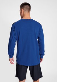Camicetta azzurra a maniche lunghe con scollatura rotonda, caratterizzata da accenti neri sulle spalle. Indossata con pantaloni corti neri, in tessuto morbido, dal taglio rilassato.