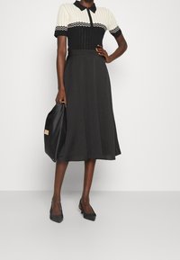 Sort kjole med en ribbet, hvid krave med bølget detaljering. Skørtet er A-formet, flyder til knæene, parret med sorte spidse hæle.