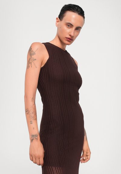 Brown ribbed dress with a sleeveless design, featuring a fitted silhouette and textured fabric. Exposed tattoo on the arm.