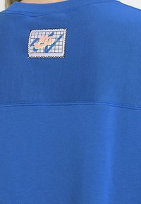 Blå sweatshirt med en rutmönstrad Nike-logotyp i brodyr på ryggen. Tillverkad av ett glatt tyg med rund hals och platt sömnadsdetalj.