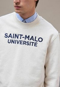 Lysfarvet sweatshirt med "SAINT-MALO UNIVERSITÉ" i marineblå broderi. Har en ribbet rund hals og indsatte ærmer.