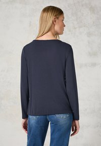 Marineblaues Langarmoberteil mit rundem Ausschnitt; glatte Textur und entspannte Passform. Getragen mit hellblauen Jeans, die einen lässigen Stil präsentieren.