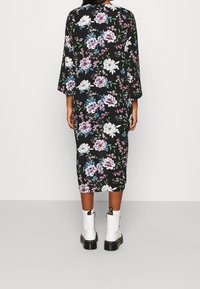 Blomstret midi kjole med trekvartærmer, sort baggrund, lilla og blå blomster, båret med hvide ankle boots. Glat tekstur.