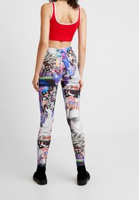 Grafiska leggings med en kollage av livliga färger och mönster, inklusive text, ansikten och abstrakta former. Bärs med en röd crop top.