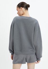 Felpa grigia oversize con orlo e polsini a coste, realizzata in morbido cotone e con una vestibilità comoda, abbinata a pantaloni corti grigi coordinati.