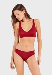 Bralette rojo sin costuras con diseño en V y tirantes anchos, combinado con braguitas altas a juego con un borde festoneado.