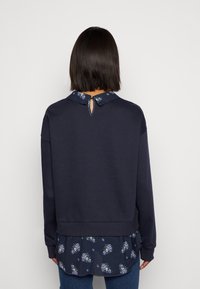 Námořnická modrá mikina s květinovým lemem a límcem, která má na zadní straně klíčovou dírku a žebrované manžety.