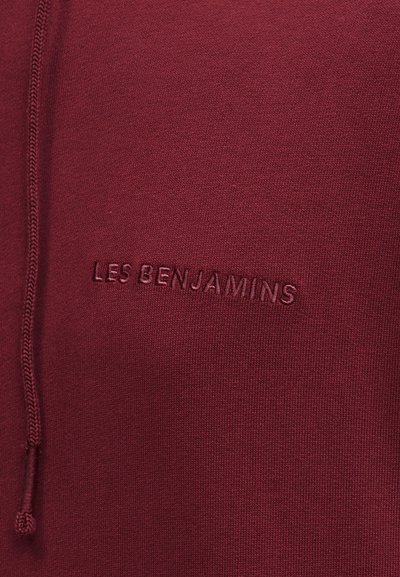 Ύφασμα μαρονού χρώματος με κεντητό κείμενο "LES BENJAMINS" στο ίδιο χρώμα και κορδόνι σύσφιξης στην αριστερή πλευρά.