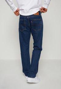 Levi's blå denimjeans med rak passform, med bakfickor och en brun läderlapp. I kombination med vita sneakers.