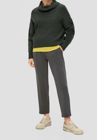 Zielony sweter o grubym splotach z wysokim kołnierzem, nałożony na żółtą bluzkę. Szare spodnie tapered i beżowe sneakersy z zielonymi akcentami.
