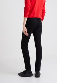 Svarta jeans i denim med slim fit och mid-rise midja, med bakfickor och subtila sömmar. Matchas med svarta slip-on skor.