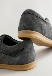 Pantofi din suede gri cu un profil jos și talpă din cauciuc maroniu deschis. Prezintă margini rotunjite și cusături subtile pe laturi.