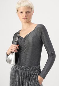 Langermet metallisk grå bodysuit med V-hals og teksturdetaljer, kombinert med en plisserte metallisk grå skjørt og en sølvveske.