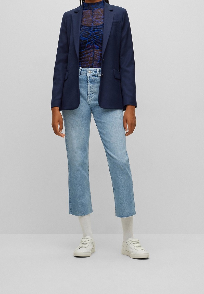 Mörkblå kavaj, blåmönstrad topp, ljusblå cropped jeans, vita sneakers och vita strumpor. Har en strukturerad design och avslappnade inslag.