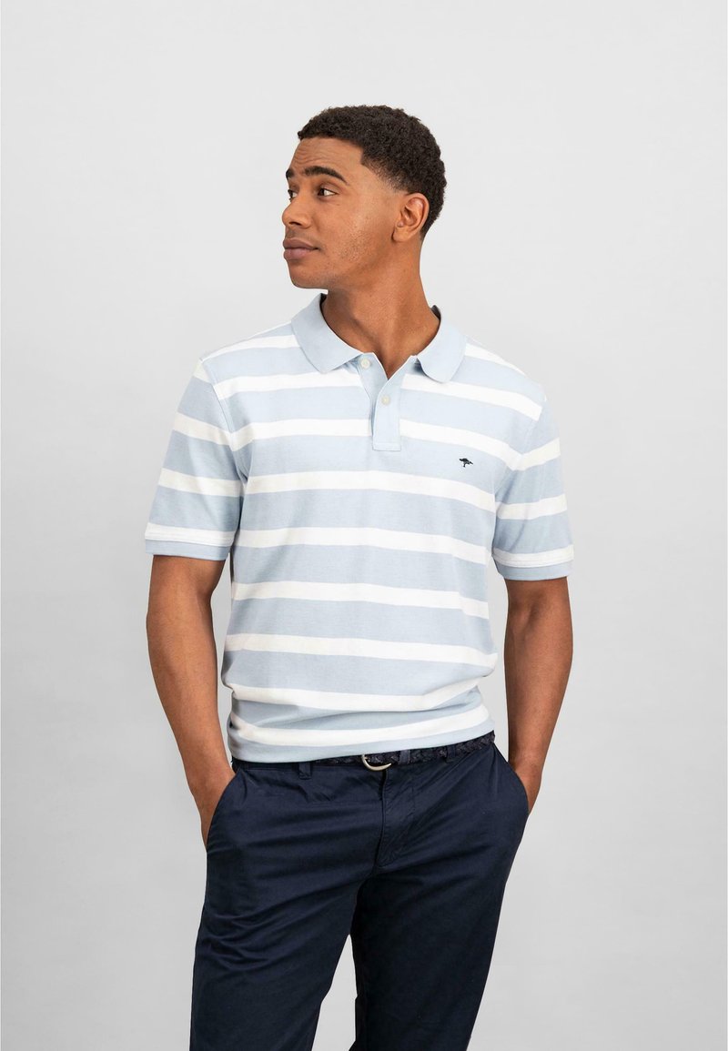 Polo rayé bleu clair et blanc avec col, manches courtes et un petit logo sur la poitrine, associé à un pantalon bleu marine foncé.