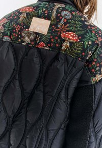 Kurtka pikowana w kolorze czarnym z kolorowym nadrukiem grzybów i liści na ramionach, z teksturowanym czarnym wnętrzem i naszywką z logo.