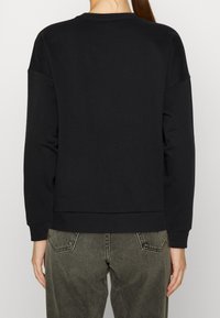 Sudadera negra con cuello redondo, hombros caídos, dobladillo acanalado y textura suave. Combinada con jeans de tiro alto en gris oscuro.
